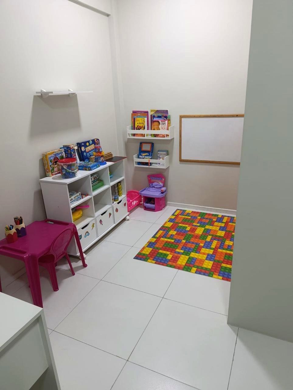 Espaço infantil com brinquedos, mesa pequena e tapete colorido