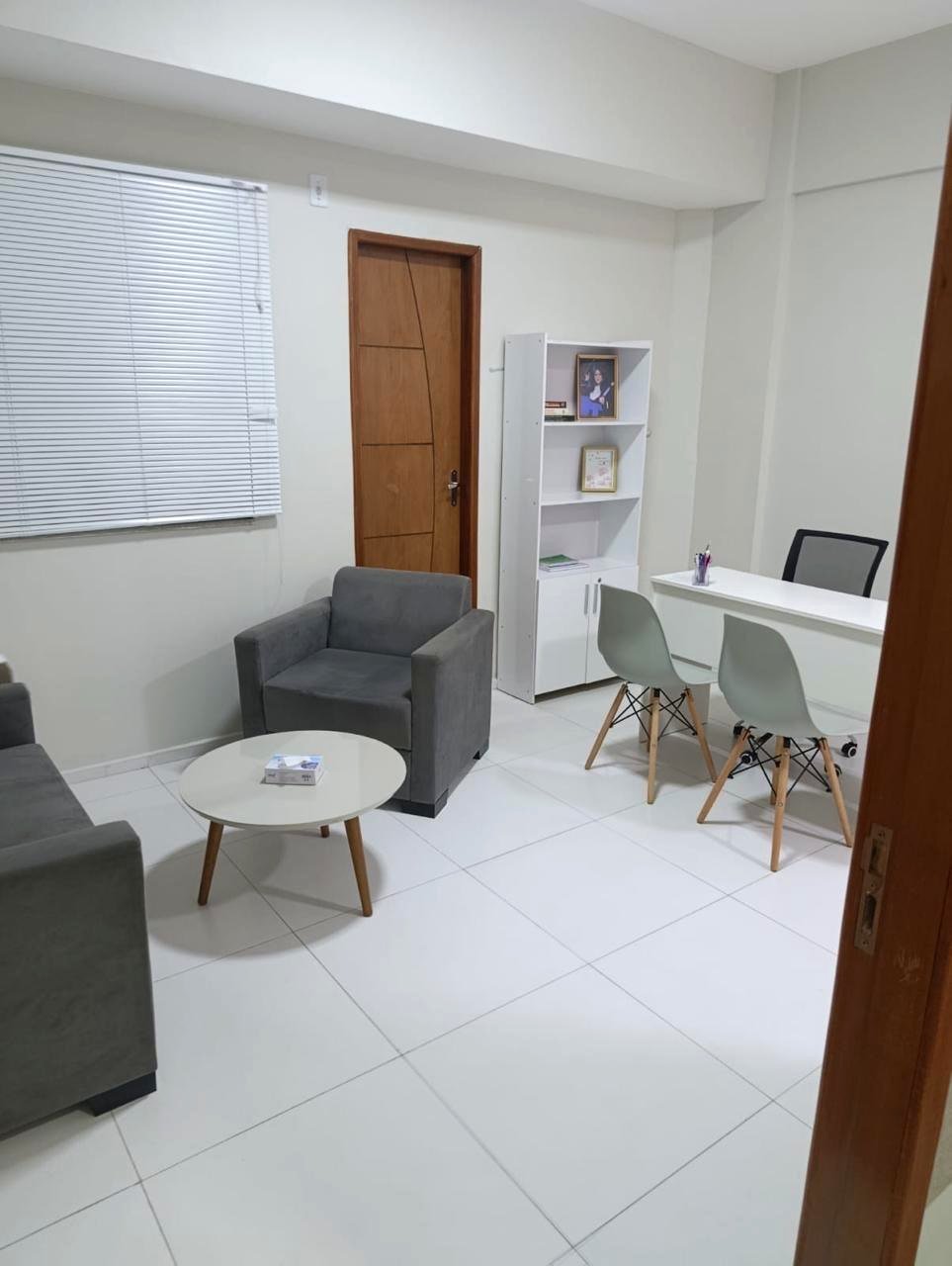 Visão geral da sala, com poltronas, mesa de apoio e estante